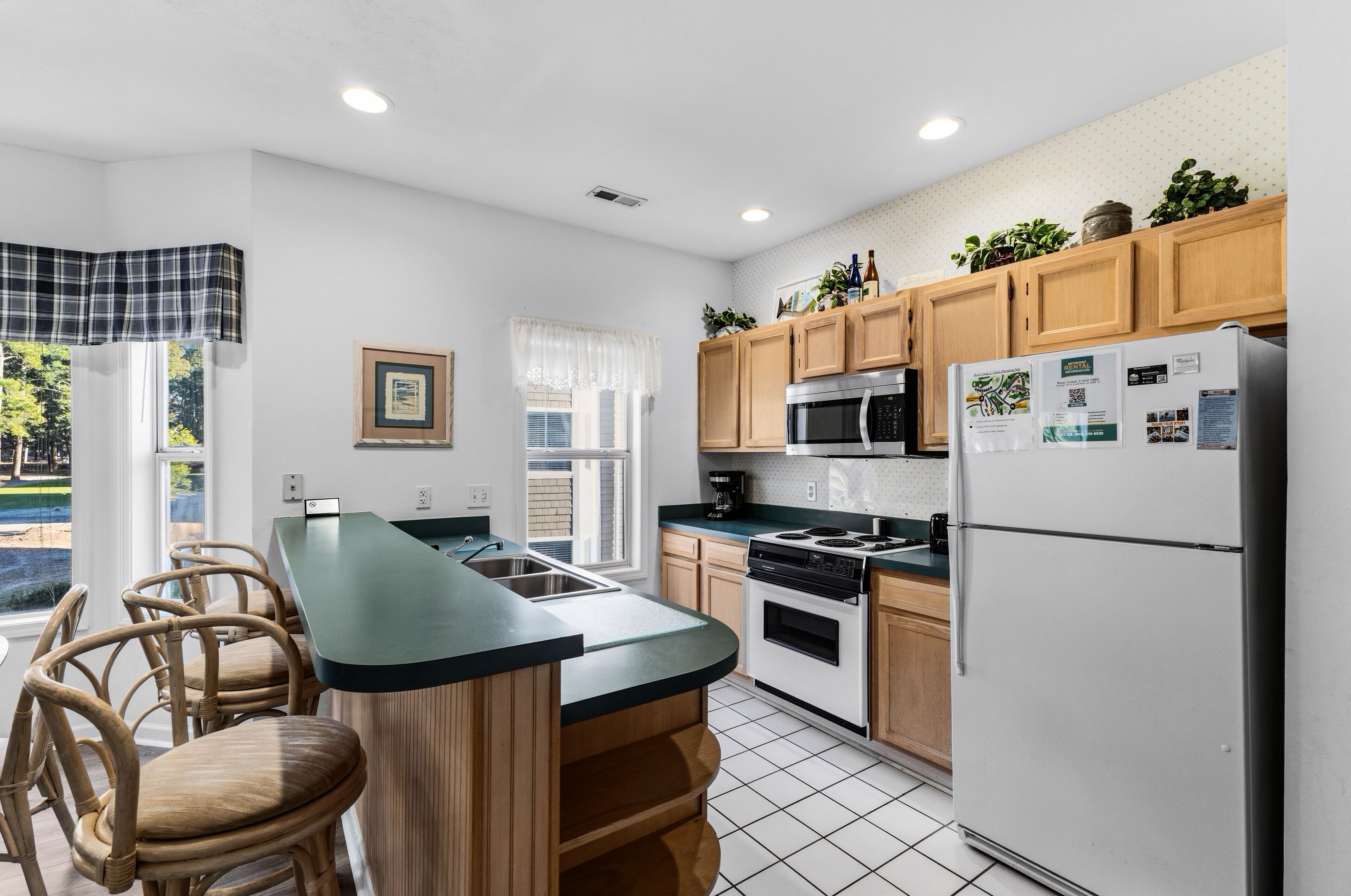 A modern kitchen with wooden cabinets, a built-in island with bar stools, a refrigerator, and a microwave.
