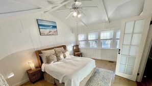 Ein Schlafzimmer mit einem großen Bett, einem Deckenventilator, einem Fenster mit Jalousien und einer Tür mit satinierten Glasscheiben.