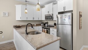 Una cocina moderna con armarios blancos, encimera de granito, electrodomésticos de acero inoxidable e iluminación colgante.
