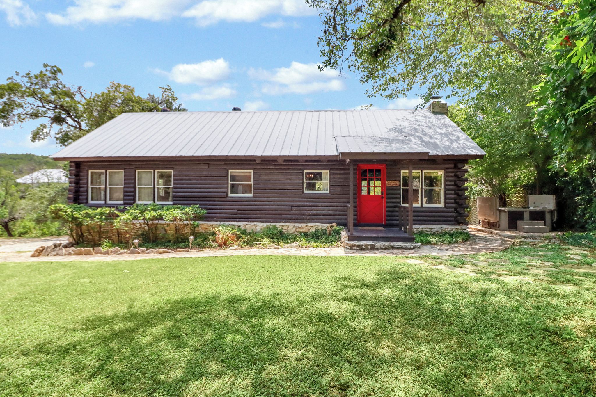 A log cabin with a red door, a stone foundation, and a grassy yard.