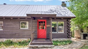 A log cabin with a red door, stone steps, and a clear water log home sign.