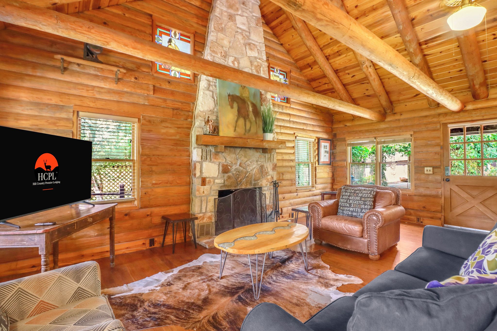 A log cabin interior with a stone fireplace, wooden furniture, and a television.