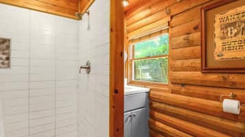 A wooden cabin bathroom with a shower, a window, and a sink.