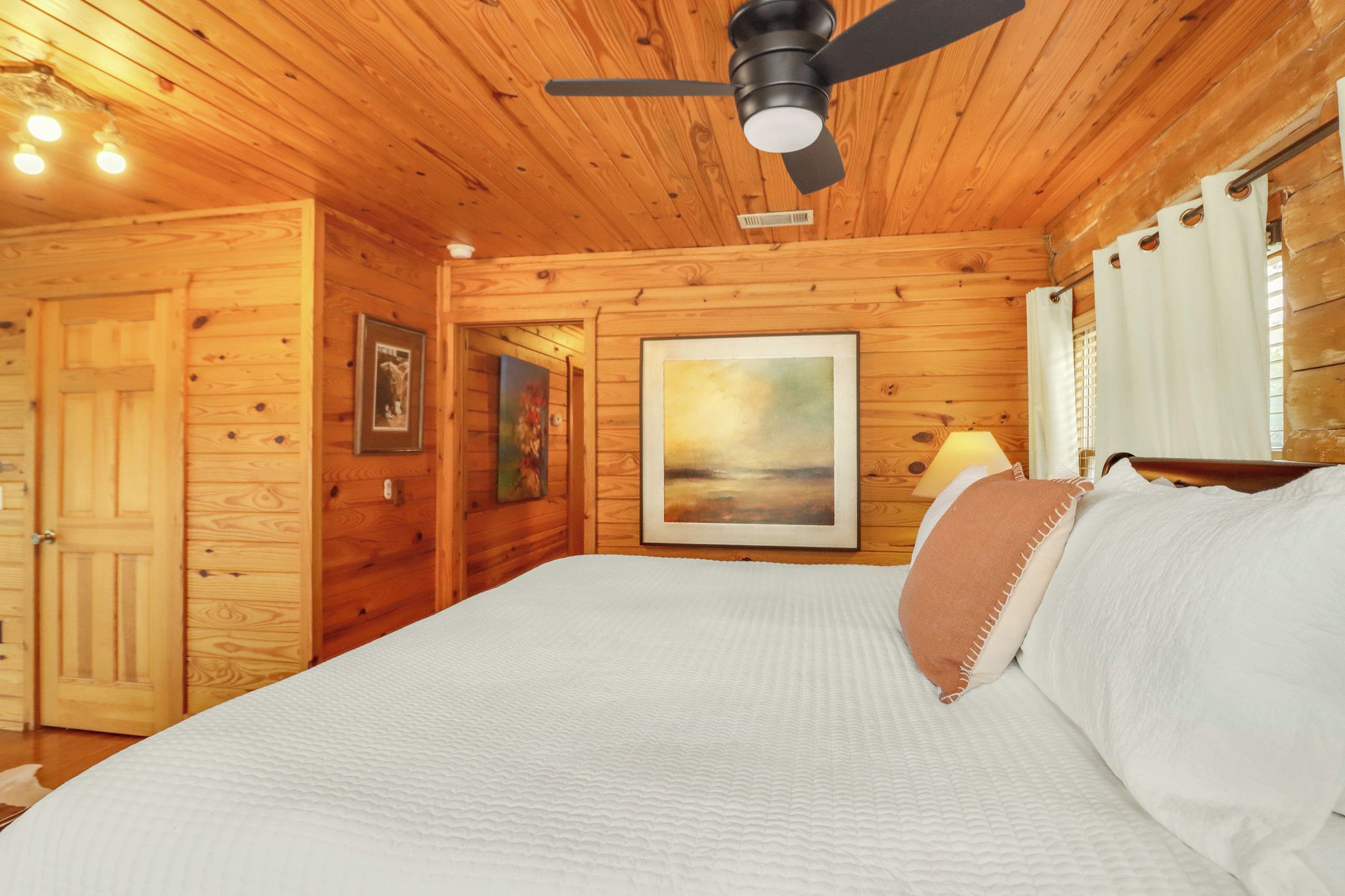 A wooden cabin bedroom with a bed, a ceiling fan, and a painting on the wall.