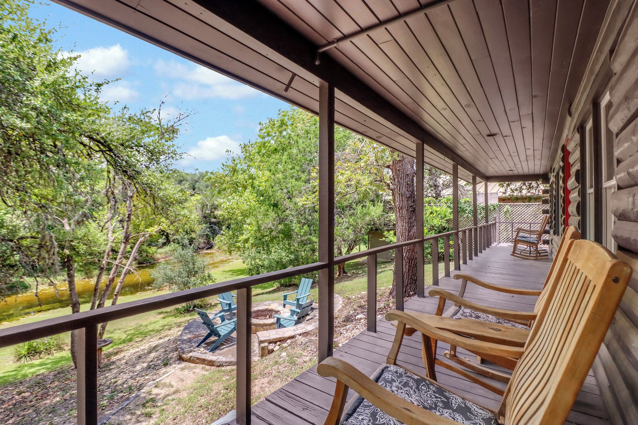 A covered outdoor deck with wooden chairs and a fire pit.