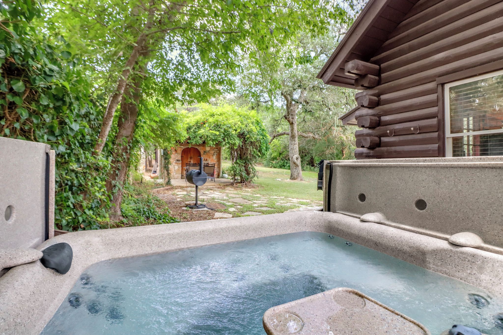 A hot tub in a garden with a wooden cabin in the background.