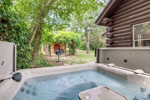 Un jacuzzi en un jardín con una cabaña de madera al fondo.
