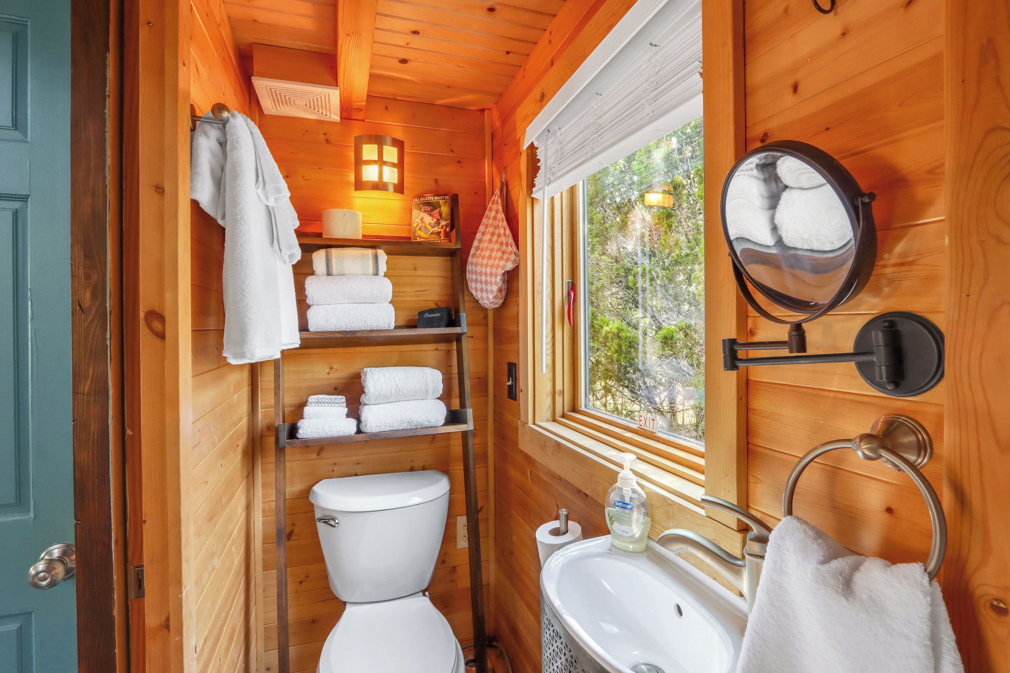 Une petite salle de bain en bois, aménagée dans une cabane, comprenant des toilettes, un lavabo et des étagères pour ranger les serviettes.