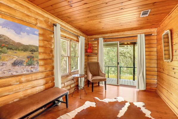 A log cabin interior with a bench, a chair, a table, and a painting of a desert landscape.