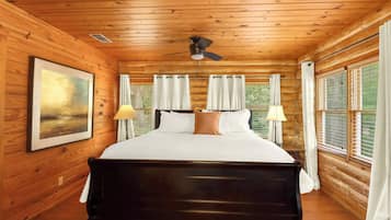 Een slaapkamer in een houten hutje met een bed, twee lampen, een plafondventilator en een raam met gordijnen.