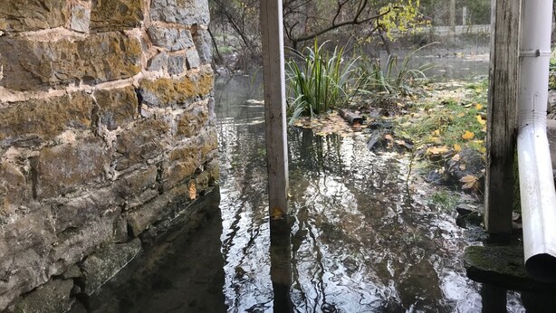 Een stenen muur naast een waterpartij, met een houten constructie en leidingen.