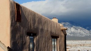 A rustic building with a unique, textured exterior, large windows, and a view of snow-capped mountains in the background.