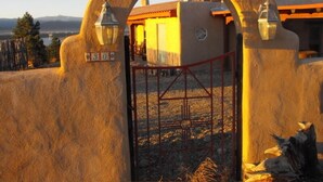 A rustic gate with a number sign, leading to a building with a tiled roof and a view of the landscape.