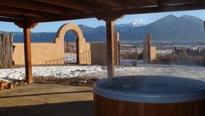 A hot tub under a wooden pergola with a view of mountains.