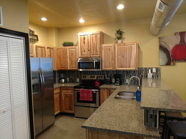 A kitchen with wooden cabinets, stainless steel appliances, granite countertops, and a tiled backsplash.