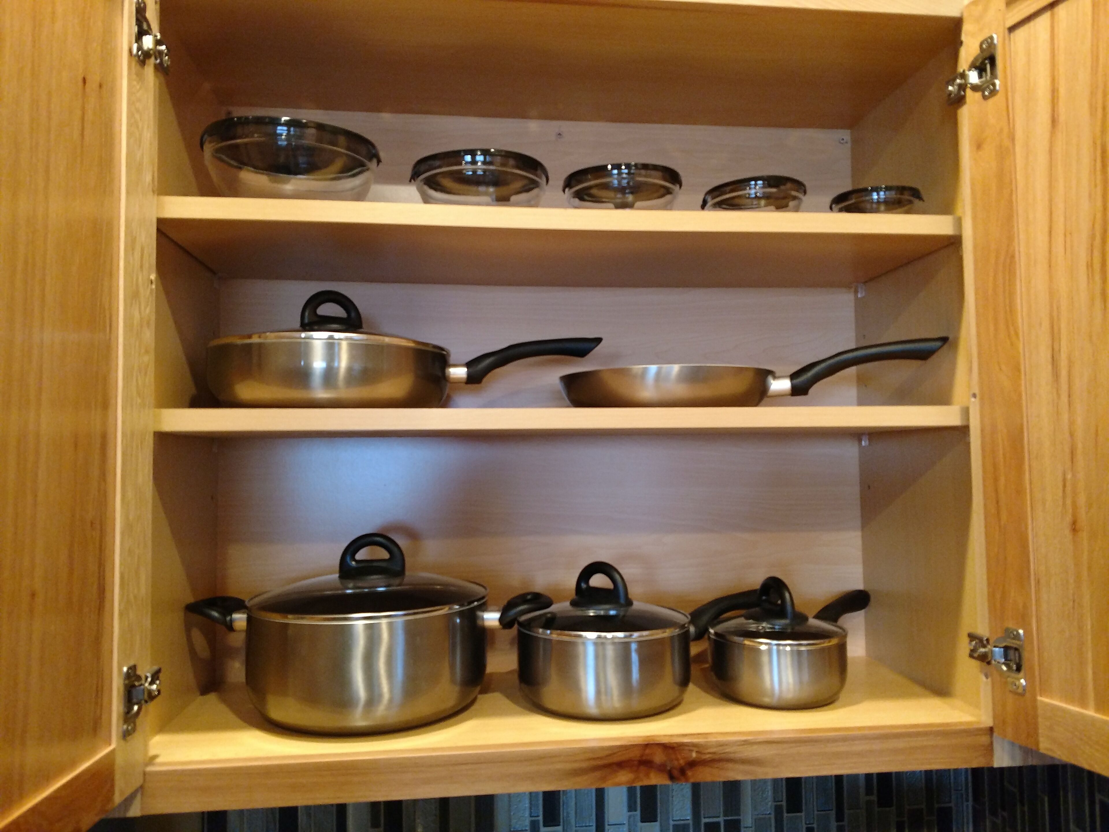A kitchen cabinet with shelves holding various cookware items.
