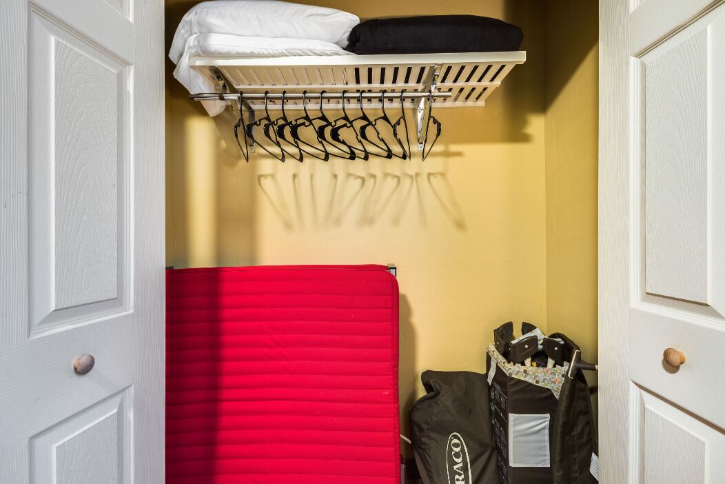 Una habitación pequeña con una cama, una manta roja, un tendedero y un neceser de artículos de aseo.