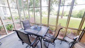 A conservatory with a table and chairs, large windows, and a view of a grassy area. - Unwind & Play | River Creek Golf Condo in NC! | RC401 (Sunset Beach)