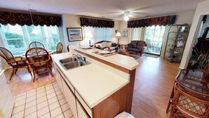 A spacious living area with a kitchen island, dining area, and seating. - Unwind & Play | River Creek Golf Condo in NC! | RC401 (Sunset Beach)
