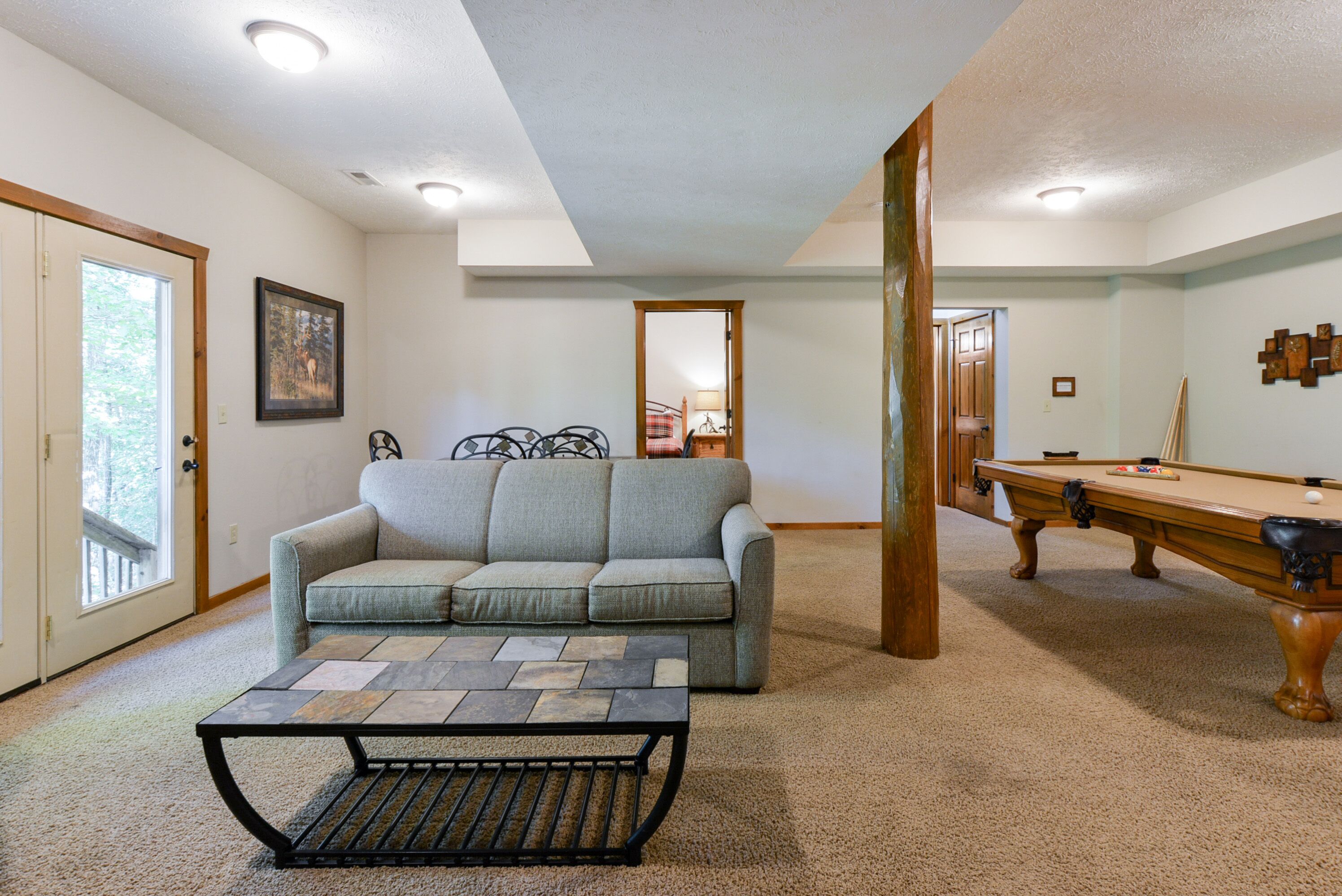 A living room with a sofa, a coffee table, a pool table, and a door leading to another room.
