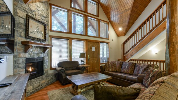 A spacious living room with a stone fireplace, a wooden coffee table, leather sofas, and a high ceiling with wooden beams. - Indoor Pool - Sleeps 22 - 8 King Beds - Right by SDC - Vanessa's Vacation Homes (Branson)