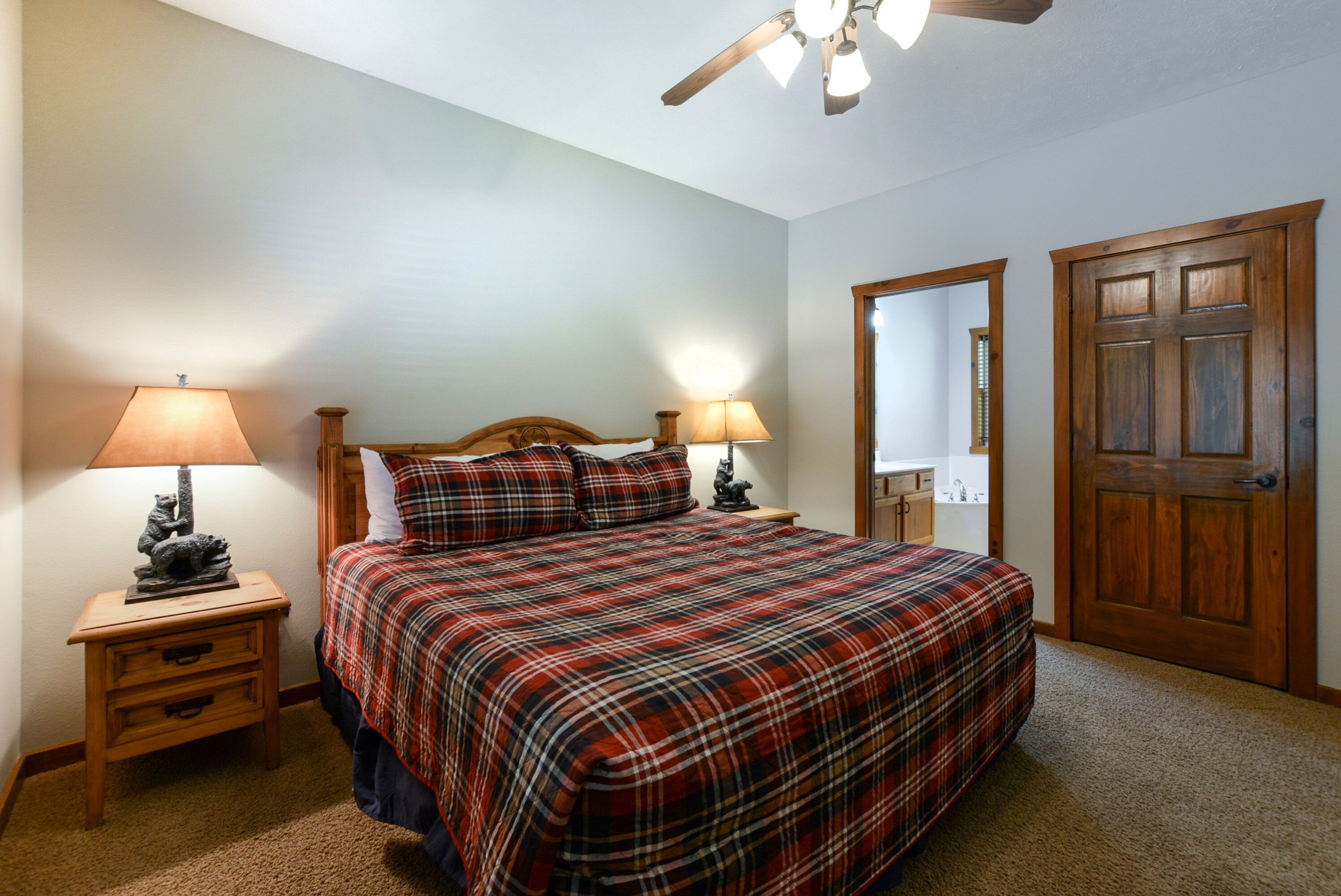 A bedroom with a bed, two bedside tables, a ceiling fan, and a wooden door.