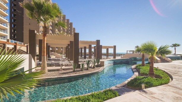 A resort pool area with clear blue water, palm trees, and a view of the ocean. - 2 Kings plus Bunk Bed Room 3rd floor Huge Patio (Puerto Penasco)