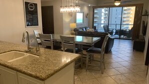 A modern kitchen with granite countertops, a dining area with a glass table, and a balcony with a view of the city. - 2 Kings plus Bunk Bed Room 3rd floor Huge Patio (Puerto Penasco)