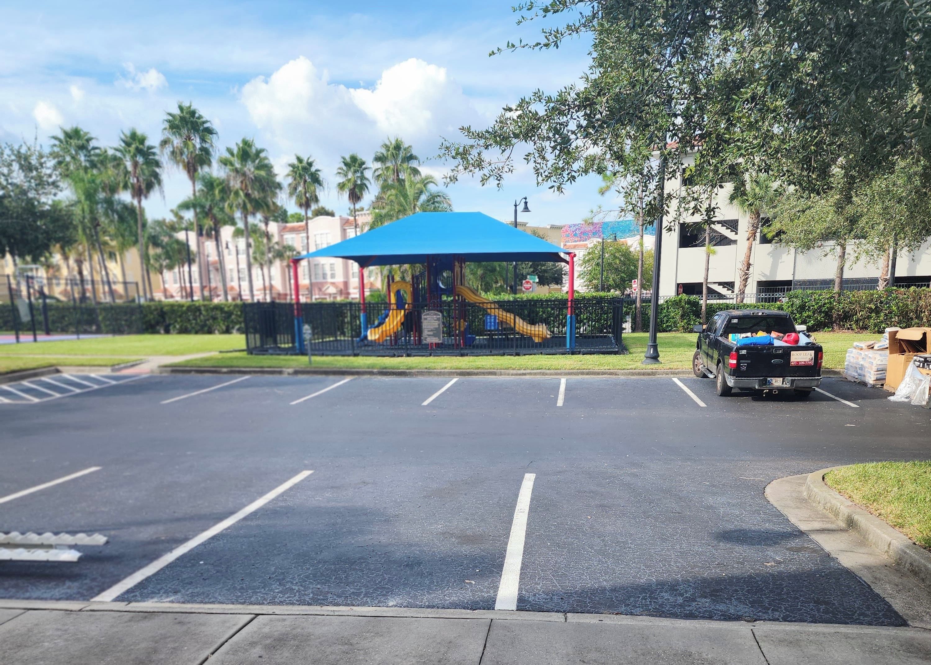 A parking lot with a playground featuring a slide and a blue canopy.