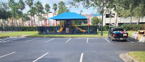 A parking lot with a playground featuring a slide and a blue canopy.