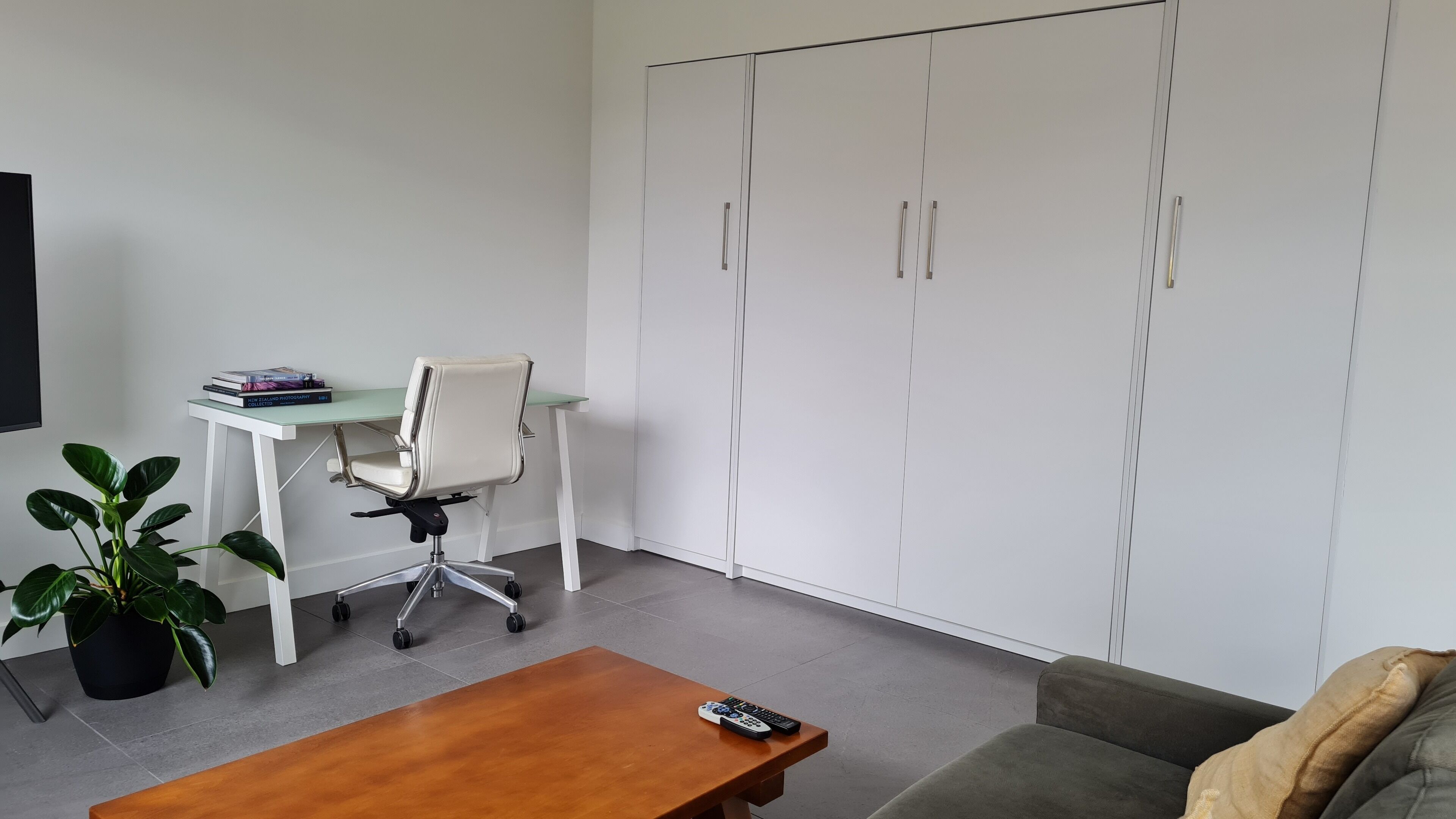 Un salon moderne avec une table basse en bois, un fauteuil de bureau blanc, un petit bureau avec des livres et une grande armoire.
