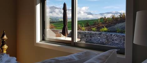 A bedroom with a large window overlooking a garden and mountains.