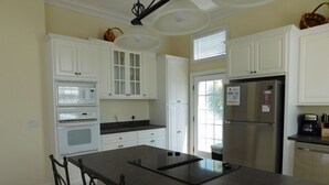 Una cocina con armarios blancos, un refrigerador de acero inoxidable, un horno empotrado y una isla grande con taburetes de bar.