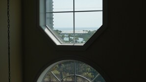 Una habitación con un tragaluz octogonal grande y una ventana circular, con vistas a una playa y un puente.