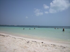 Ein Strand mit klarem türkisblauem Wasser, einem sandigen Ufer und ein paar badenden Personen.