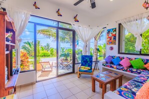 Ein Zimmer mit einer großen Schiebetür und einem Balkon, ein farbenfrohes Sofa, ein Holzstuhl und ein kleiner Tisch.