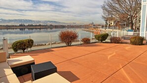 Eine Terrasse mit Gartenmöbeln, Blick auf einen See und ein Gebirge im Hintergrund.