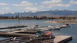 Un port de plaisance avec des bateaux amarrés, une jetée en bois et, en arrière-plan, des montagnes aux sommets enneigés.