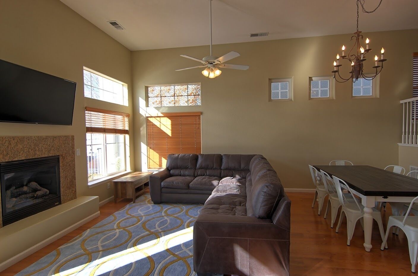 A living room with a fireplace, a large sectional sofa, a dining table with chairs, and a chandelier.