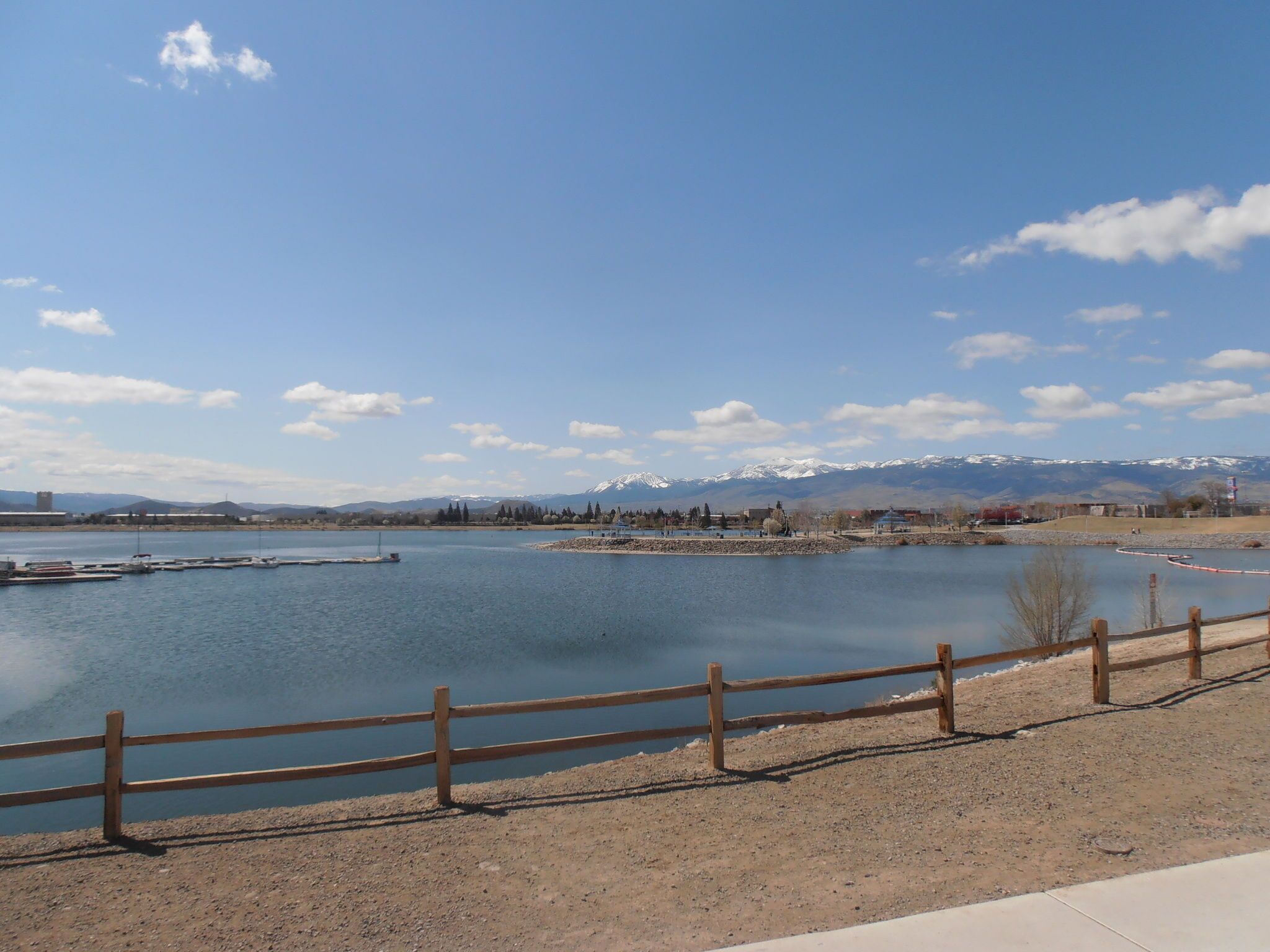Vista lacustre con valla de madera, un muelle y montañas al fondo.