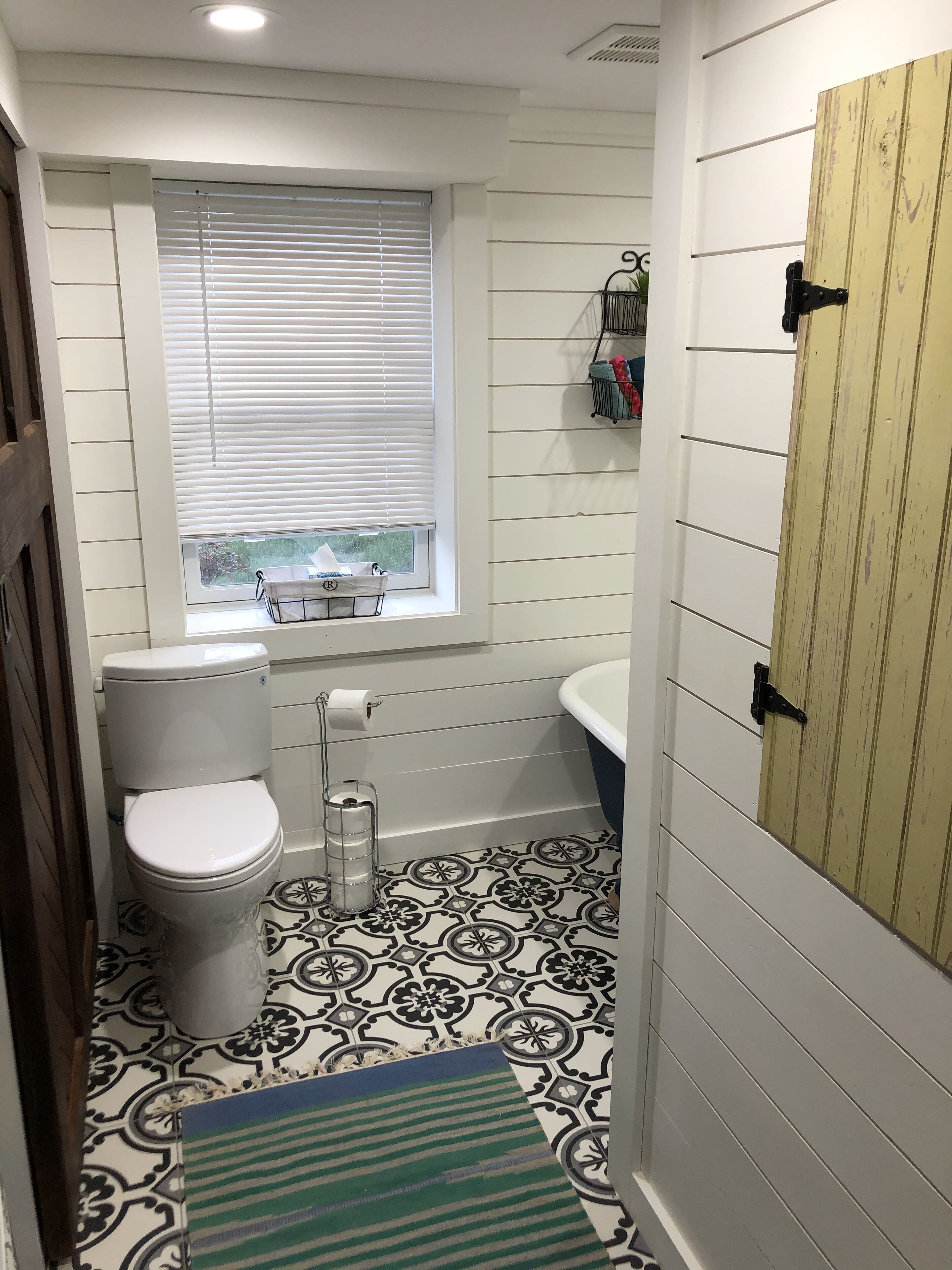 A bathroom with a toilet, a window with blinds, a bathtub, and a shower area.