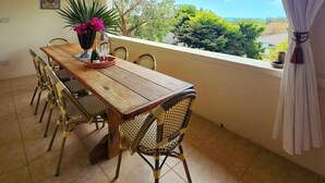 Un comedor con mesa de madera y sillas de mimbre, una planta en maceta y vistas al exterior.