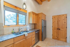 Una cocina con armarios de madera, un refrigerador de acero inoxidable, una encimera de granito, una ventana con persianas y una puerta de madera.