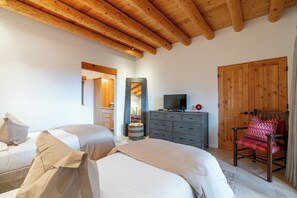 Un dormitorio con techo de madera, cama, cómoda, televisor y una silla.