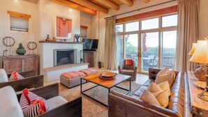 A cozy living room with a fireplace, comfortable seating, and a large window offering a view. - Bishop's Lodge Villa 43D | Views & Luxury (Santa Fe)
