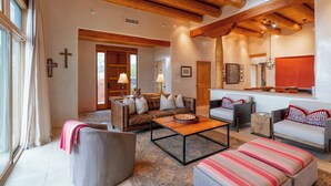 A spacious living room with a high wooden ceiling, a fireplace, and a large window. - Bishop's Lodge Villa 43D | Views & Luxury (Santa Fe)