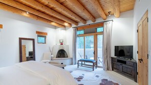A bedroom with a bed, a fireplace, a television, and a large window with curtains. - Bishop's Lodge Villa 43D | Views & Luxury (Santa Fe)