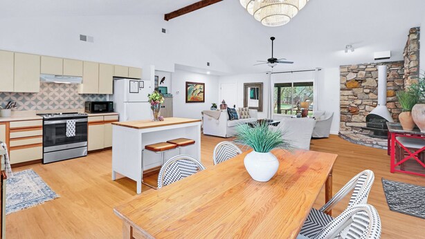 A modern kitchen with white cabinets, a wooden dining table, and a stone fireplace. - Darling Cottage with access to 2 Blanco River Parks! (Wimberley)