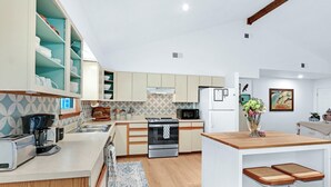 A modern kitchen with white cabinets, a microwave, a stove, and a sink. There is a wooden island with two stools and a vase of flowers. - Darling Cottage with access to 2 Blanco River Parks! (Wimberley)