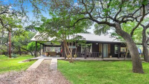 A building with a covered porch, surrounded by trees and a gravel path. - Darling Cottage with access to 2 Blanco River Parks! (Wimberley)